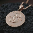 Load image into Gallery viewer, Rose gold plated heraldic eagle coin pendant necklace presented on textured volcanic stone, showcasing the crowned eagle crest and coin-inspired relief in a refined macro studio shot.