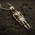 Load image into Gallery viewer, Bronze Ra amulet pendant necklace resting on black volcanic stone, featuring an ancient Egyptian deity figure with a falcon-like head, sun disk, and strong sculpted body in a detailed macro product photograph.