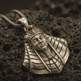 Load image into Gallery viewer, Bronze Tutankhamun pendant necklace resting on black volcanic stone, featuring the iconic Egyptian pharaoh bust with detailed nemes headdress and cobra crown in a macro product photograph.