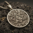 Load image into Gallery viewer, Bronze Eye of Providence pendant necklace with an oxidized finish resting on textured volcanic rock, captured in a close-up premium studio composition.