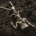 Load image into Gallery viewer, Bronze Baphomet pendant necklace with an oxidized finish resting on textured volcanic rock, captured in a close-up premium studio composition.
