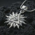 Load image into Gallery viewer, Polished silver Eye of Providence sun pendant necklace displayed on black volcanic rock, shown in a refined macro product shot with triangular eye symbol and radiant flame-like sun rays.