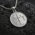 Load image into Gallery viewer, Polished silver Venus Amor pendant necklace displayed on black volcanic rock, shown in a refined macro product shot with goddess figure, symbolic motifs, and engraved medallion detail.