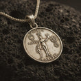 Load image into Gallery viewer, Bronze Venus Amor pendant necklace with an oxidized finish resting on textured volcanic rock, captured in a close-up premium studio composition.