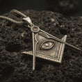 Load image into Gallery viewer, Bronze Master Mason pendant necklace with an oxidized finish resting on textured volcanic rock, captured in a close-up premium studio composition.