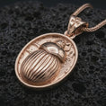 Load image into Gallery viewer, Rose gold plated Egyptian scarab pendant necklace on dark volcanic rock, photographed in a detailed premium studio macro view.