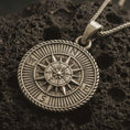 Load image into Gallery viewer, Bronze steampunk compass pendant necklace with an oxidized finish resting on textured volcanic rock, captured in a close-up premium studio composition.
