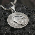 Load image into Gallery viewer, Polished silver Spartan helmet pendant necklace displayed on black volcanic rock, shown in a refined macro product shot with Greek key border, warrior profile, and classical armor detail.