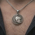 Load image into Gallery viewer, Oxidized Spartan helmet pendant necklace worn on the neck, styled in a dark lifestyle portrait with an open shirt and masculine presentation.