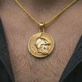 Load image into Gallery viewer, Gold plated Spartan helmet pendant necklace worn on the neck, captured on a human model in a premium dark-toned lifestyle frame.
