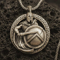 Load image into Gallery viewer, Bronze Spartan warrior pendant necklace with an oxidized finish resting on textured volcanic rock, captured in a close-up premium studio composition.