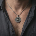 Load image into Gallery viewer, Oxidized compass rose pendant necklace worn on the neck, styled in a dark lifestyle portrait with an open shirt and masculine presentation.