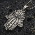 Load image into Gallery viewer, Sterling silver Hamsa hand pendant necklace with an oxidized finish resting on textured volcanic rock, captured in a close-up premium studio composition.