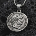 Load image into Gallery viewer, Oxidized Emperor Augustus coin pendant necklace resting on black volcanic stone, featuring a Roman imperial side profile with laurel wreath and engraved ancient lettering in a detailed macro product photograph.