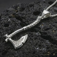 Load image into Gallery viewer, Polished silver battle axe pendant necklace displayed on black volcanic rock, shown in a refined macro product shot with engraved blade details and wrapped handle design.