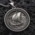 Load image into Gallery viewer, Sterling silver Viking ship pendant necklace with an oxidized finish resting on textured volcanic rock, captured in a close-up premium studio composition.