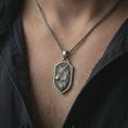 Load image into Gallery viewer, Oxidized wolf shield pendant necklace worn on the neck, styled in a dark lifestyle portrait with an open shirt and bold masculine presentation.