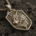 Load image into Gallery viewer, Bronze wolf shield pendant necklace with an oxidized finish resting on textured volcanic rock, captured in a close-up premium studio composition.