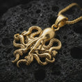 Load image into Gallery viewer, Gold plated octopus pendant necklace presented on porous volcanic rock, highlighting the sea creature silhouette in a luxurious close-up jewelry image.