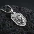 Load image into Gallery viewer, Polished silver ferocious wolf shield pendant necklace displayed on black volcanic rock, shown in a refined macro product shot with aggressive wolf head relief, layered fur detail, and angular shield frame.