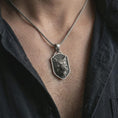 Load image into Gallery viewer, Oxidized ferocious wolf shield pendant necklace worn on the neck, styled in a dark lifestyle portrait with an open shirt and bold masculine presentation.
