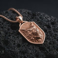 Load image into Gallery viewer, Rose gold plated ferocious wolf shield pendant necklace on dark volcanic rock, photographed in a detailed premium studio macro view.