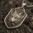 Load image into Gallery viewer, Bronze fox shield pendant necklace with an oxidized finish resting on textured volcanic rock, captured in a close-up premium studio composition.