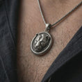 Load image into Gallery viewer, Oxidized lioness pendant necklace worn on the neck, styled in a dark lifestyle portrait with an open shirt and bold elegant presentation.