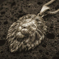 Load image into Gallery viewer, Bronze lion head pendant necklace with an oxidized finish resting on textured volcanic rock, captured in a close-up premium studio composition.
