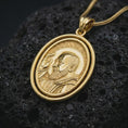 Load image into Gallery viewer, Gold plated Saint Padre Pio spinning pendant necklace photographed on porous black volcanic stone, emphasizing the Catholic saint relief and elegant rotating medallion design in a luxury jewelry composition.