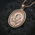 Load image into Gallery viewer, Rose gold plated Saint Padre Pio spinning pendant necklace presented on textured volcanic stone, showcasing the sacred portrait, oval spinner structure, and refined devotional detailing in a macro studio shot.