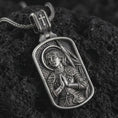 Load image into Gallery viewer, Oxidized Joan of Arc dog tag pendant necklace resting on black volcanic stone, featuring a detailed saint warrior portrait with halo, folded hands, and armor in a devotional sterling silver design.