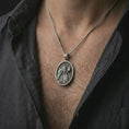 Load image into Gallery viewer, Oxidized Good Shepherd Jesus pendant necklace worn on the chest, close-up lifestyle jewelry photo showing the religious medallion on a spiga chain with dark clothing.
