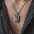 Load image into Gallery viewer, Oxidized Saint Francis pendant necklace worn on the chest, close-up lifestyle jewelry photo showing the religious medallion on a spiga chain with dark clothing.