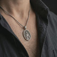 Load image into Gallery viewer, Oxidized Saint Francis pendant necklace worn on the chest, close-up lifestyle jewelry photo showing the religious medallion on a spiga chain with dark clothing.