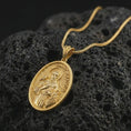 Load image into Gallery viewer, Gold plated Saint Francis pendant necklace on textured volcanic rock, premium close-up studio composition emphasizing the saint figure, bird, and wolf symbolism.