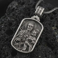 Load image into Gallery viewer, Oxidized Saint Joseph and Jesus pendant necklace on textured volcanic rock, close-up studio shot highlighting the father and child relief, lily, sacred heart, and antique silver contrast.