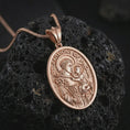 Load image into Gallery viewer, Rose gold plated Saint Anthony of Padua pendant necklace on textured volcanic rock, detailed macro product shot with soft warm reflections and devotional Saint Anthony design.