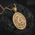 Load image into Gallery viewer, Gold plated Saint Anthony of Padua pendant necklace on textured volcanic rock, premium close-up studio composition emphasizing the saint holding baby Jesus and lily symbolism.