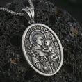 Load image into Gallery viewer, Oxidized Saint Anthony of Padua pendant necklace on textured volcanic rock, close-up studio shot highlighting the saint and child relief, lily detail, halo, and antique silver contrast.