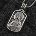 Load image into Gallery viewer, Oxidized Saint James the Apostle pendant necklace on textured volcanic rock, close-up studio shot highlighting the apostle relief, halo, book detail, and antique silver contrast.