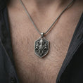 Load image into Gallery viewer, Oxidized kraken octopus shield pendant necklace worn on the neck, styled in a dark lifestyle portrait with an open shirt and bold ocean-inspired presentation.