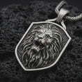 Load image into Gallery viewer, Sterling silver roaring lion shield pendant necklace with an oxidized finish resting on textured volcanic rock, captured in a close-up premium studio composition.