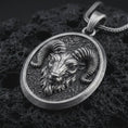 Load image into Gallery viewer, Sterling silver ram head pendant necklace with an oxidized finish resting on textured volcanic rock, captured in a close-up premium studio composition.