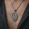 Load image into Gallery viewer, Oxidized Our Lady of Guadalupe spinner pendant necklace worn on the chest, close-up lifestyle jewelry photo showing the Catholic medallion on a spiga chain with dark clothing.