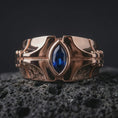 Load image into Gallery viewer, A sterling silver ring with a rose gold plated finish and marquise blue stone displayed on textured volcanic rock in a premium macro shot.