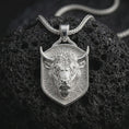 Load image into Gallery viewer, Polished silver bull head shield pendant necklace displayed on black volcanic rock, shown in a refined macro product shot with sharp horns, intense facial sculpting, and geometric shield frame.