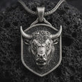 Load image into Gallery viewer, Sterling silver bull head shield pendant necklace with an oxidized finish resting on textured volcanic rock, captured in a close-up premium studio composition.