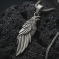 Load image into Gallery viewer, Sterling silver raven pendant necklace with an oxidized finish resting on textured volcanic rock, captured in a close-up premium studio composition.