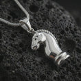 Load image into Gallery viewer, Polished silver knight chess piece pendant necklace displayed on black volcanic rock, shown in a refined macro product shot with sculpted horse head profile, smooth contours, and minimalist game-inspired design.